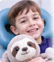 Niño sonriente en el sillón dental abrazando un peluche